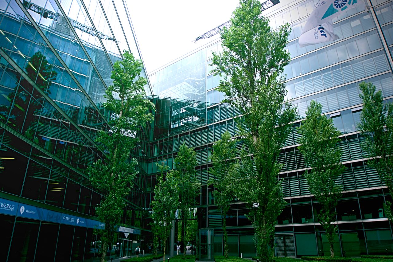 Contemporary glass architecture with trees reflecting in the facade on a bright day.