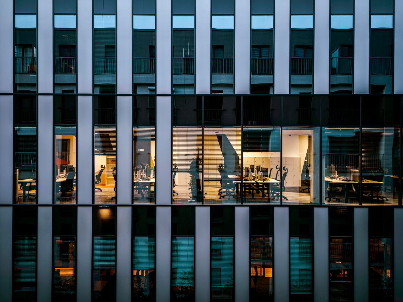 about-img Illuminated office inside a modern glass building exterior, showcasing architecture and workspace design.