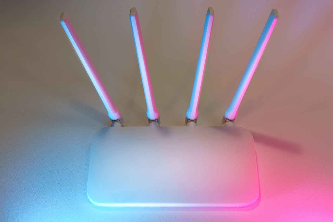 programs-01 Sleek white wireless router with four antennas emitting soft blue and pink light.